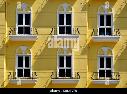 Gelbe Fassade einer Wohnanlage mit sechs Fenstern und Balkons mit dramatischen Schatten in Singapur Stockfoto