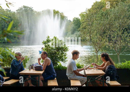 Personen, die am späten Nachmittag Sonnenschein am Pavillon Cafe, das von West Lake, Victoria Park, East London, Großbritannien Stockfoto