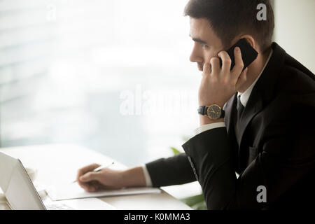 Ernsthafte Geschäftsmann sprechen auf Zelle am Schreibtisch sitzen, Seite portra Stockfoto
