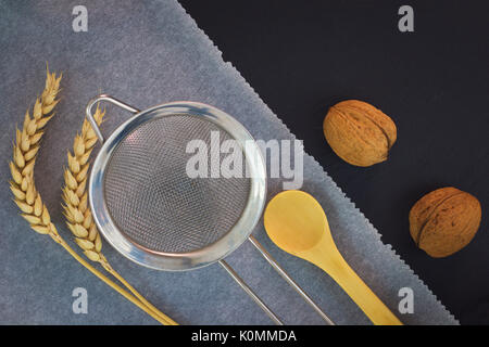 Essen Werkzeuge vorbereiten Für backen in der Bäckerei - Mehl oder Zucker Filter, Holz Kaffee Löffel, Backpapier, Walnüsse und Weizenähren auf schwarzem Schiefer Platte Stockfoto