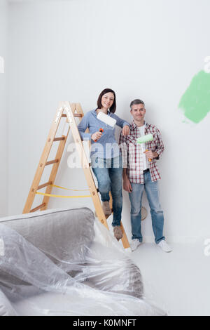 Glückliches junges Paar ihre Startseite und Malerei Zimmer renovieren, sind sie posiert mit Farbe rollen und lächelnd Stockfoto