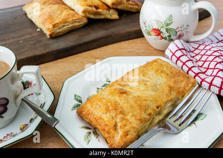 Anzeige von Apfelkuchen mit einer Tasse Tee und einen Krug Milch. Mehr Gebäck im Hintergrund auf einem hölzernen display board Stockfoto