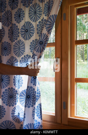 Hand öffnet Vorhang auf die hölzerne Ferienhaus Haus Fenster. Helles Sonnenlicht durchscheint. Schönen Sommermorgen Licht hinter dem Fenster Stockfoto