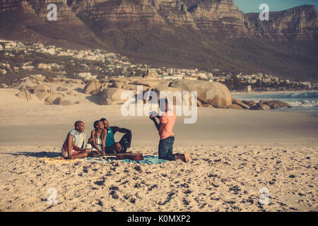 Afrikanische jungen Mann Freunde fotografieren per Telefon im Freien am Strand. Schöner Mann, der seine Freunde vom Smartphone. Stockfoto
