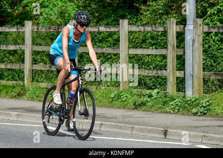 Eine Radfahrerin, die mit Geschwindigkeit auf einer Straße in Newquay in Cornwall fährt. Stockfoto