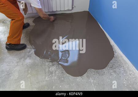 Arbeitnehmer stellt ein fließestrich mit Kelle auf Betonboden im Haus Stockfoto