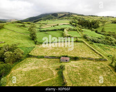 Luftaufnahme von grünem Farmland und einem kleinen vulkanischen Felsen Hütte und Wände in der Nähe von Lajes, einem Dorf auf der Insel Flores in Portugal. Stockfoto