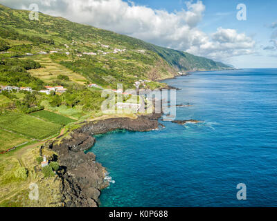Luftaufnahme zeigt das kleine Dorf Manadas und dem blauen Wasser des Atlantischen Ozeans auf Sao Jorge, Portugal. Stockfoto