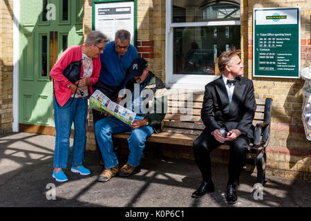 Ein Mann sitzt auf einer Bank ausserhalb Lewes Bahnhof Blick auf einer Karte und die Leute auffordern, für Wegbeschreibungen, Lewes, Sussex, UK Stockfoto