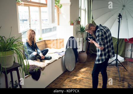 Fotograf Fotografieren weibliche Mode Modell sitzen auf alkovenfenster Sitz im Studio Stockfoto