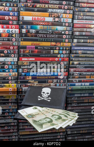 Gestapelte DVD-Filme & Schwarz pirate Portemonnaie und Chinesischen Renminbi Banknoten. Metapher der Chinesischen Urheberrecht IP-Diebstahl, US-China trade Krieg, China Piraterie. Stockfoto