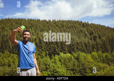 Junger Mann unter selfie beim Stehen gegen Bäume während der sonnigen Tag Stockfoto