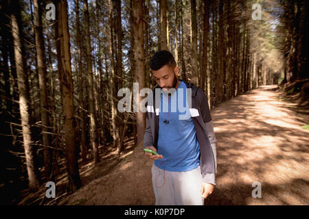 Mann mit Handy beim Gehen auf der Straße inmitten von Bäumen im Wald Stockfoto