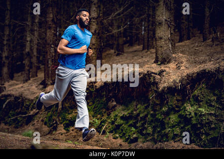 Low Angle View junger Mann laufen von Bäumen im Wald Stockfoto