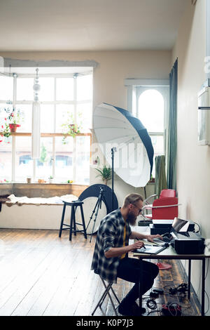 Seitenansicht des Fotografen mit Grafiktablett während der Bearbeitung am Tisch im Studio Stockfoto