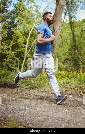 Seitenansicht des jungen Mannes Joggen auf der Straße im Wald Stockfoto