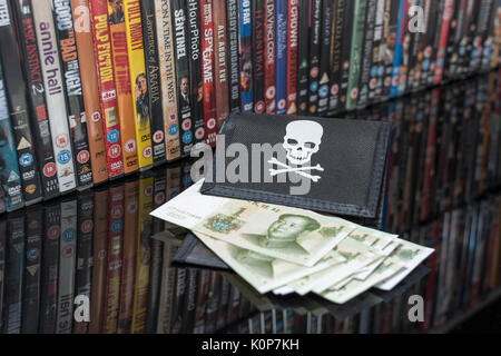 Gestapelte DVD-Filme & Schwarz pirate Portemonnaie und Chinesischen Renminbi Banknoten. Metapher der Chinesischen Urheberrecht IP-Diebstahl, US-China trade Krieg, China Piraterie. Stockfoto