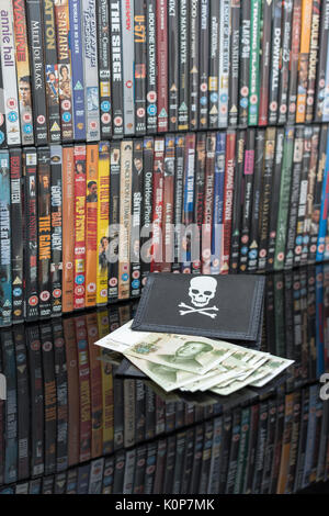 Gestapelte DVD-Filme & Schwarz pirate Portemonnaie und Chinesischen Renminbi Banknoten. Metapher der Chinesischen Urheberrecht IP-Diebstahl, US-China trade Krieg, China Piraterie. Stockfoto