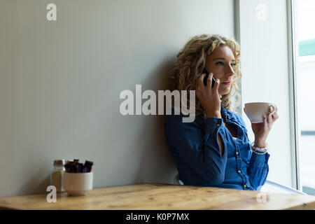 Frau am Telefon sprechen, während Kaffee am Tisch im Cafe Stockfoto