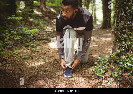 Der Mensch auf der Suche beim Binden an den Schuhbändern in Wald Stockfoto