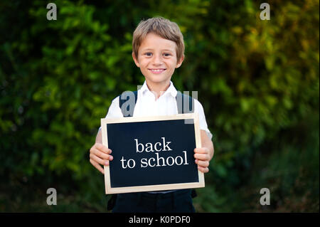 Zurück zum Konzept der Schule. Volksschule student boy Holding blackboard Hintergrund. Cute kaukasischen primäre Klasse Schüler in für den ersten Tag in der Ausbildung Semester Stockfoto