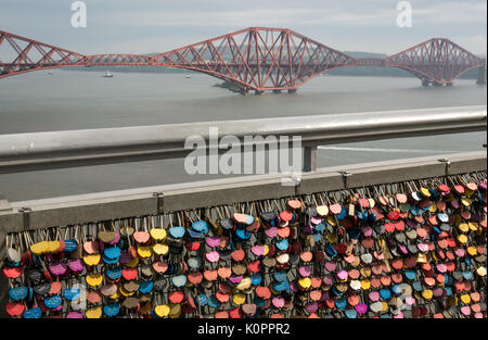 Abschnitt der Brücke Geländer mit Masse an bunten Liebe Sperren auf Gehweg Geländer der Forth Road Bridge mit Forth Rail Bridge in Distanz, Schottland, Großbritannien Stockfoto