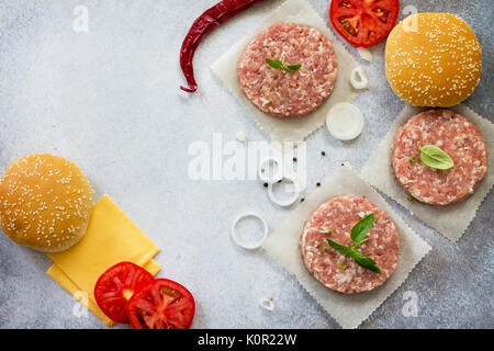 Zutaten für Cheeseburger - rohes Schnitzel, Brötchen, Käse, Zwiebeln, Gewürze, Gemüse und Tomaten. Street Food, Fast Food. Ansicht von oben mit einer Kopie. Stockfoto