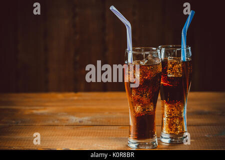 Schöne kalte Getränke von Cola mit Eiswürfeln mit einem Kessel Strohhalme in Gläsern auf hölzernen Hintergrund mit freier Speicherplatz Stockfoto