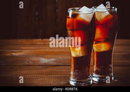 Schöne kalte fizzy cola Soda mit Würfeln Eis in Gläser Becher auf alten Holz- Hintergrund mit freier Speicherplatz Stockfoto