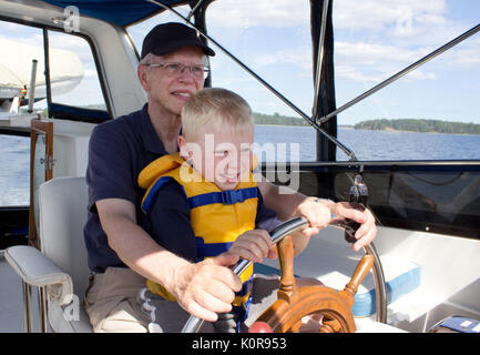 Ein älterer Mann hält seine Enkel, das Tragen einer Schwimmweste, wie Sie ein Boot aus dem Ruder lenken Stockfoto