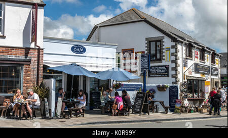 Menschen außerhalb ein Cafe/Restaurant sitzen und andere Fore Street entlang zu laufen, in dem kleinen Touristenort Tintagel, Cornwall, England, Großbritannien. Stockfoto