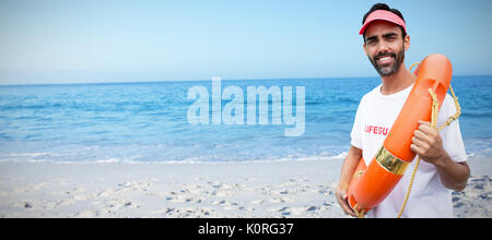 Portrait der männlichen Rettungsschwimmer holding Rettungsring gegen Strand gegen den klaren Himmel Stockfoto