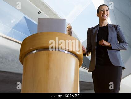 Digital composite der Geschäftsfrau auf dem Podium sprechen an Konferenz mit architektonischen Perspektive Hintergrund Stockfoto