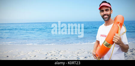 Portrait der männlichen Rettungsschwimmer holding Rettungsring gegen Strand gegen den klaren Himmel Stockfoto