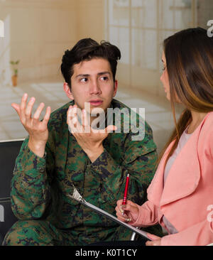 Stattliche unglücklichen jungen Soldaten Uniform tragen, leiden Posttraumatische Belastungsstörungen nach dem Krieg, im Gespräch mit den Therapeuten in einem medizinischen Zentrum, in einem entgratet Hintergrund Stockfoto