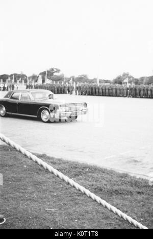 Schwarzes Auto, mit Fahne, Fahren auf einer Straße vorbei an eine große Gruppe von Soldaten an Aufmerksamkeit, Bild von Seite der Straße genommen, hinter roped weg, Vietnam, 1969. Stockfoto