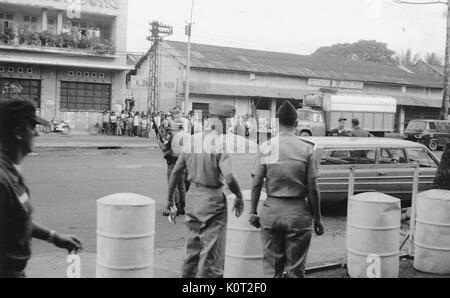 Amerikanische Soldaten versammelt auf einer Straße nach der Bombardierung der Stadt Nghe An, Ky-Son, Autos, große Gruppe von vietnamesischen Bürger stehen auf der gegenüberliegenden Seite der Straße, während des Vietnam Krieges, 1966. Stockfoto