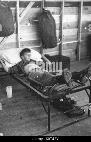 Ein United States Army Veteran Festlegung auf die Federn von einem Bett ohne Matratze abdecken, Duffel Bags hängen von den Mauern der Kaserne sind während ein Ablagefach und Stiefel auf dem Boden, Vietnam, 1967 gesehen werden kann. Stockfoto