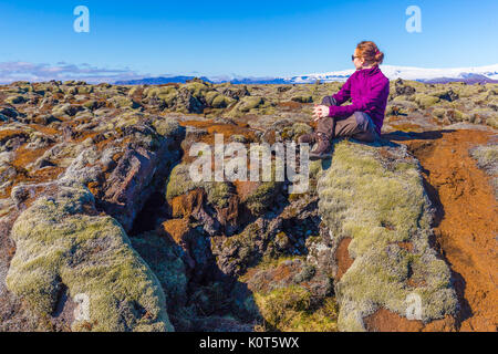 Junge Frau Wanderer auf Felsen an bemoosten Lavafeld in der Nähe von Vik, Island sitzen Stockfoto