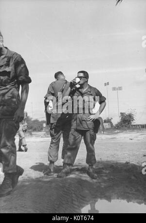 Eine kleine Gruppe von Soldaten zusammen draußen versammelt, ein Soldat ist das Trinken aus einem Pappbecher, Gebäude und große Richtantennen im Hintergrund, Vietnam, 1967 gesehen werden kann. Stockfoto