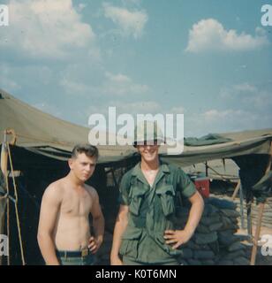 Zwei United States Army Soldaten posieren für ein Foto, während in Vietnam stationiert, der Soldat auf der linken Seite ist nicht das Tragen von einem T-Shirt und der Soldat auf der rechten Seite trägt seine volle Uniform und einen Helm, Vietnam, 1968. Stockfoto