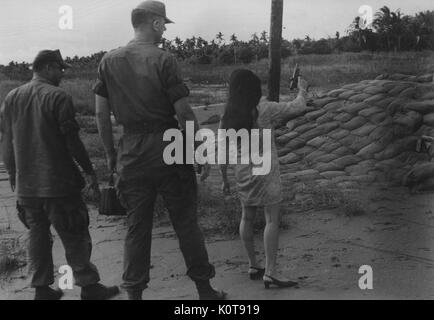 Eine Pistole lodert und wirft eine Schale nach einer Vietnamesin Brände während zwei US-Marines hinter ihr zusehen, während der Vietnamkrieg, Vietnam, 1965. Stockfoto