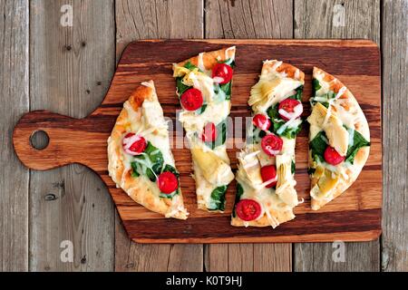 Gesunde Fladenbrot Pizza mit geschmolzenem Mozzarella, Tomaten, Spinat und Artischocken, oben Blick auf Holz paddle Board Stockfoto