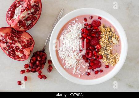 Smoothie Schüssel mit Granatäpfel, Himbeeren, Kokos und Müsli, Overhead Szene auf Marmor Stockfoto