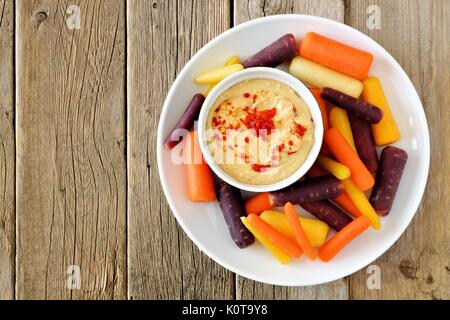 Platte mit Baby rainbow Karotten mit Hummus dip, Ansicht von oben auf einem rustikalen Holzmöbeln Hintergrund Stockfoto