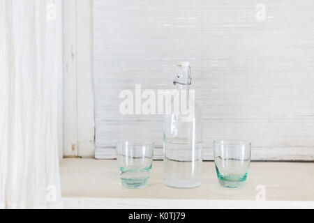Ein transparentes Glas Flasche und zwei Cup für Wasser auf weißem Hintergrund. Wodka zu trinken