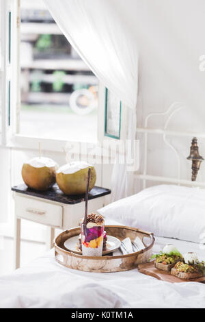 Frische leckere Frühstück im Bett auf Holz fach Joghurt mit Früchten und Chia, Honig Pfannkuchen, zwei Toasts mit Avocado und pochierte Eier und zwei Junge cocon Stockfoto