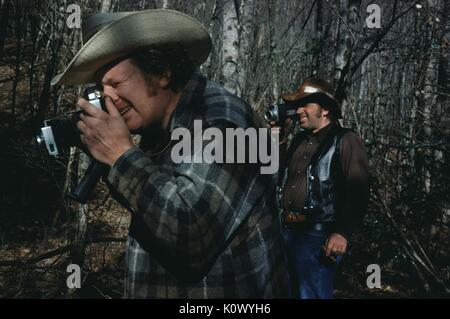 Zwei Jäger im Wald, in Flanell und Cowboyhüte gekleidet, eine durch das Objektiv einer 35-mm-Kamera suchen, die anderen Blick durch die Linse eines 8-mm-Film Film Kamera, umgeben von Bäumen, geröstete Körner Creek, Kentucky, 1975. Photo credit Smith Collection/Gado/Getty Images. Stockfoto