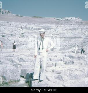 Seemann in United States Navy uniform, stehend mit den Händen an den Hüften vor der Ruine eines römischen Amphitheater, anderen Touristen im Hintergrund über Kameras, Fotos zu machen, Athen, Griechenland, 1967. Photo credit Smith Collection/Gado/Getty Images. Stockfoto