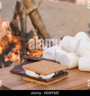 Smores Zutaten an einem Strand mit Lagerfeuer mit Schokolade, Eibisch, und Graham Cracker mit Raum für Kopie Stockfoto